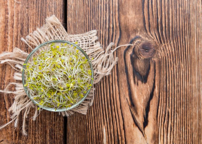 Top down view of broccoli sprouts in a glass bowl on a wooden table