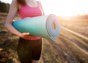 Woman holding a yoga mat with sun shining behind her