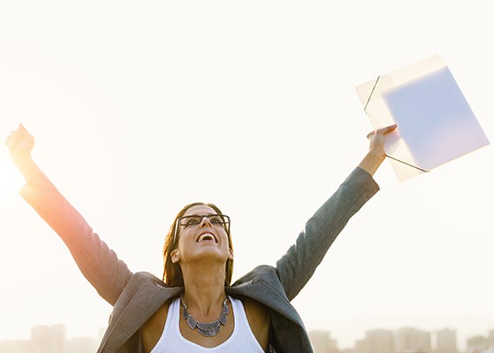 Woman in business attire and a folder in her hand celebrating a win at work