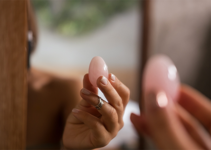 Woman holding up a pink yoni egg to a mirror