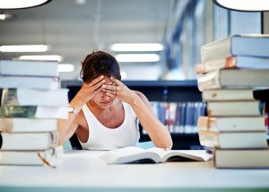 Woman with head in her hands behind a pile of books