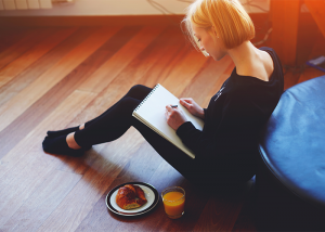 Woman sitting on the floor journaling with breakfast