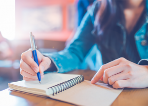 Close up of woman holding her pen to her notebook journaling