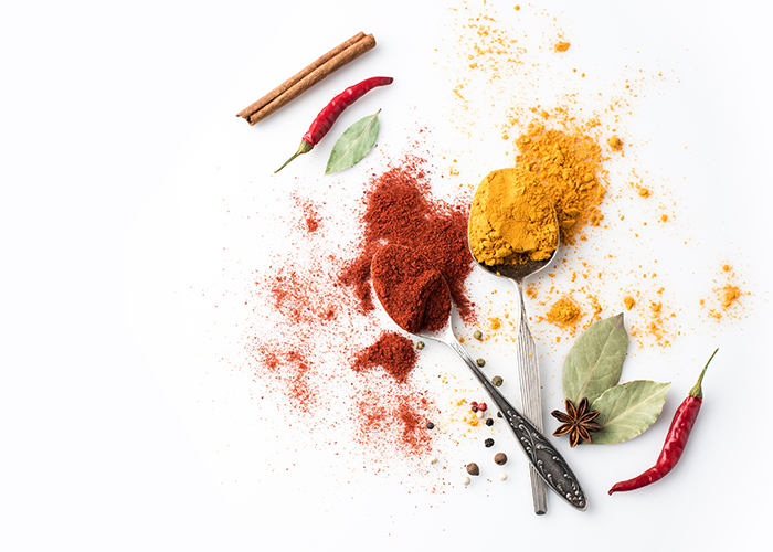 Top down view of spice powders on tablespoons, and fresh spices laid out on a white surface