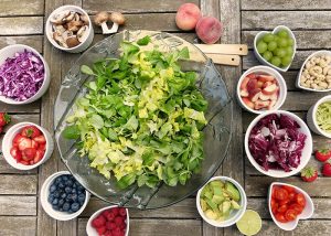 top down view of a big bowl of green salad in the middle, with small white bowls surrounding it filled with other fresh fruits and vegetables