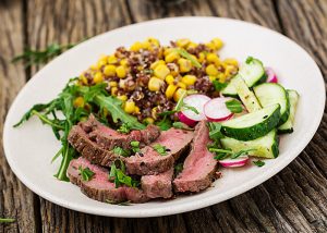 White plate topped with a corn, cucumber and radish salad and a small portion of lean red meat