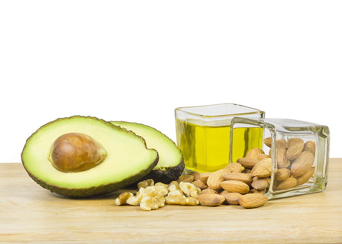 Two halved avocados, nuts, and olive oil in a small square glass bowl on a wooden table