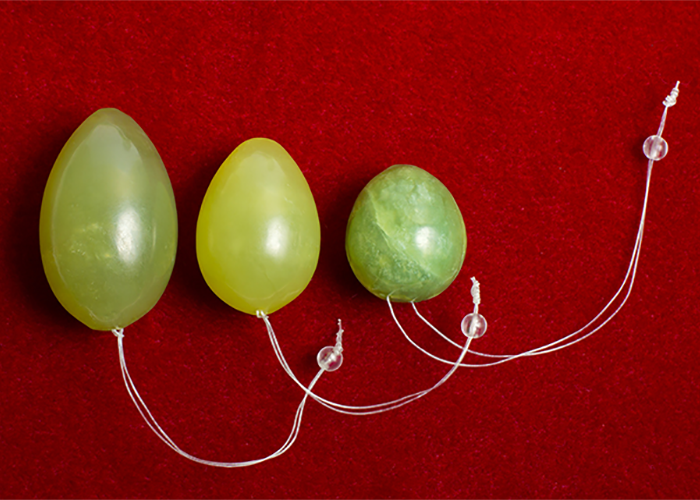 Three green and gold jade yoni eggs  with strings on a red background