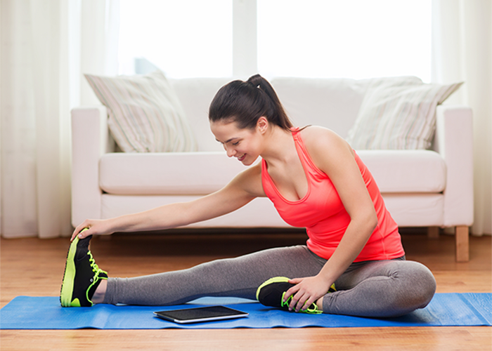 Woman doing stretching at home on a yoga mat with instructions from workout app for women