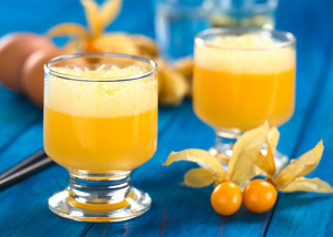 Two glasses of golden berry smoothie with a couple of golden berries next to it on a blue table.