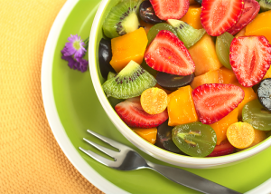 Golden berries on top of a colorful bowl of fruit salad with kiwi, strawberries, melons, and grapes.