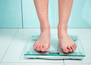 Close up of woman's legs standing on a weight scale in the bathroom.