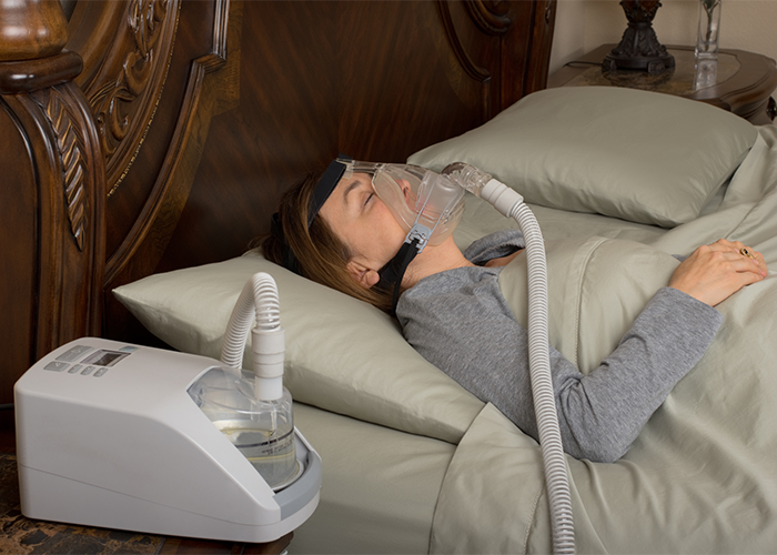 Woman in bed wearing a CPAP as she sleeps in bed.