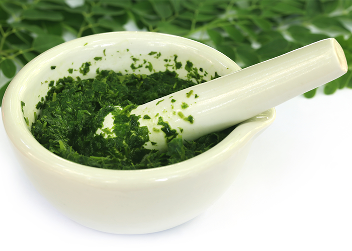 Moringa leaves ground up in a mortar with a pestle on top
