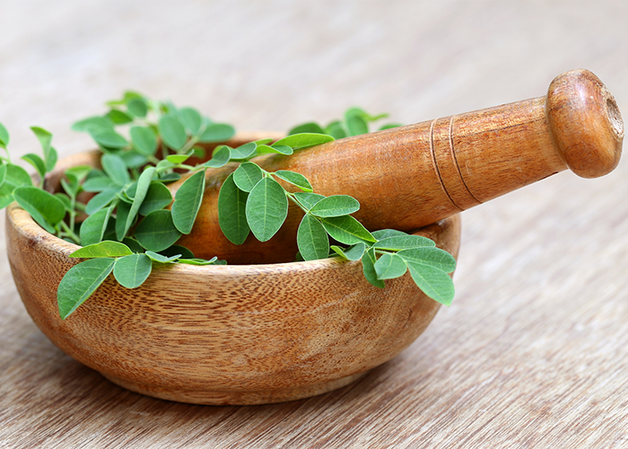 Moringa leaves in a mortar with a pestle on top