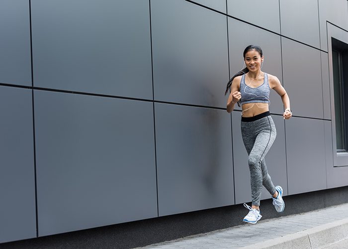 Young woman running for weight loss next to a grey wall