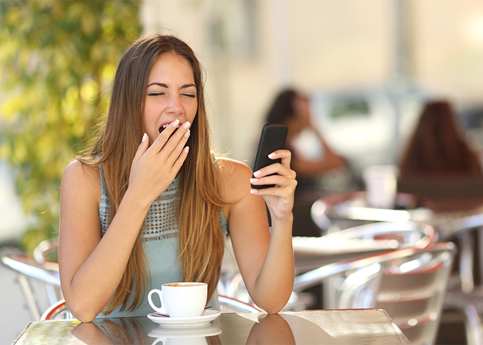 Pretty woman with sleep disorder tired during the day and yawning at an outdoor cafe while having a coffee.