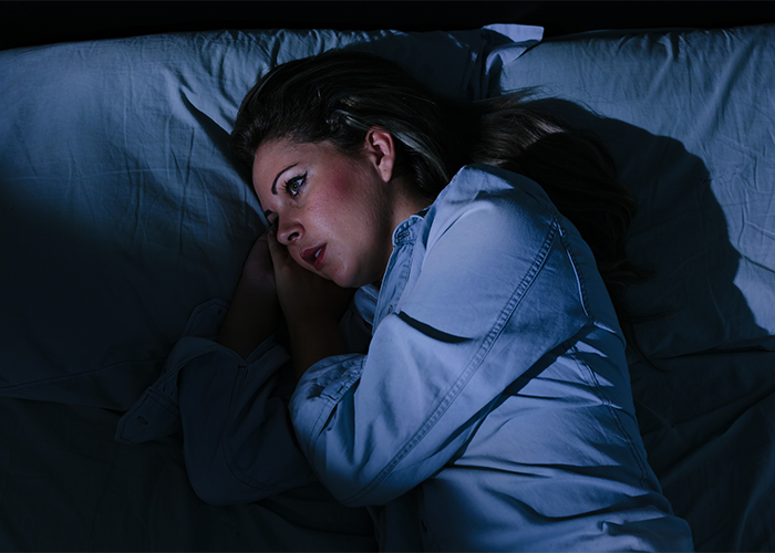 Woman with insomnia lying awake in bed in a dark room.