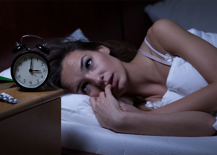 Woman with sleep disorder lying awake in bed with her alarm clock showing 3AM.
