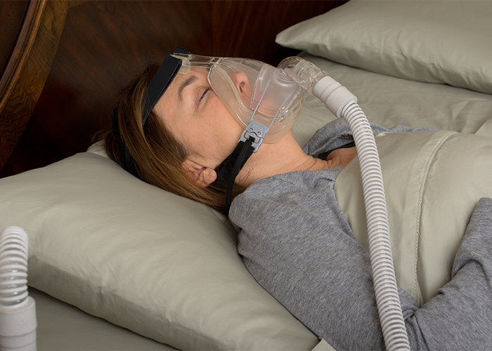 Woman lying in bed sleeping with CPAP machine on.