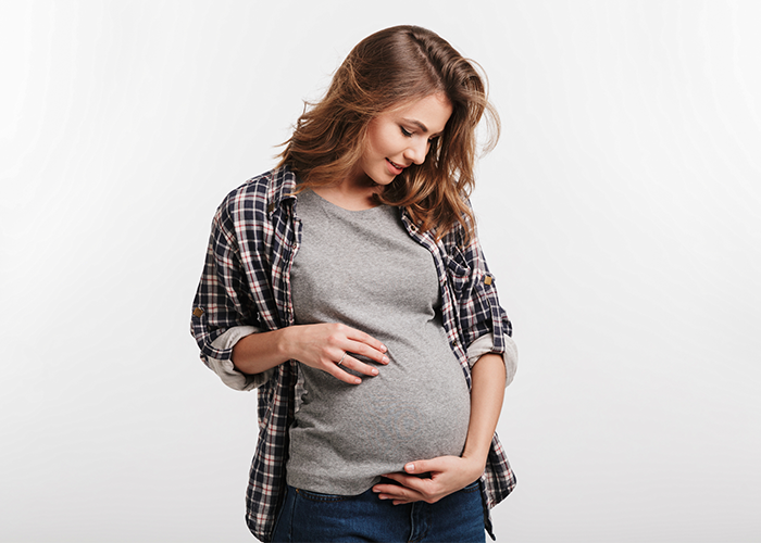 30-year-old pregnant woman in a flannel shirt holding her belly