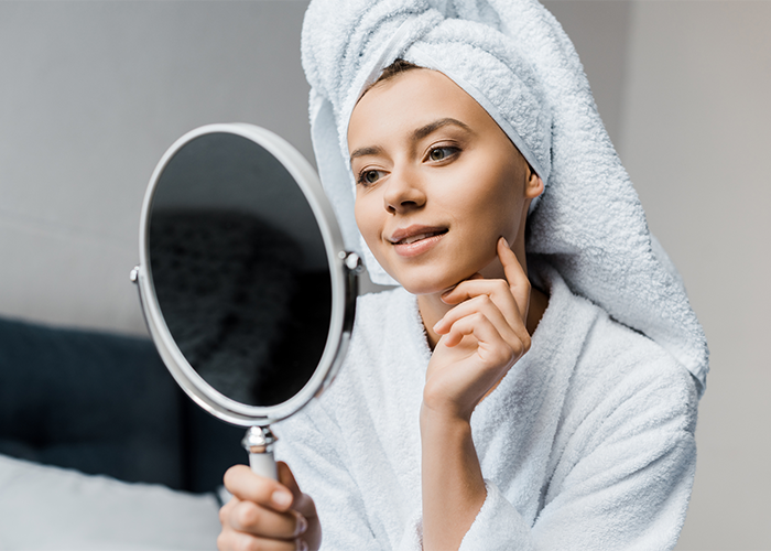30-year-old woman in a bathrobe looking at her face in a beauty mirror
