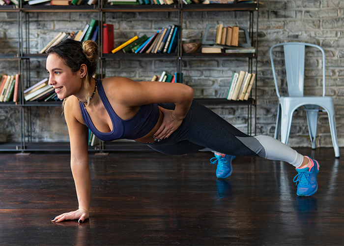 Woman doing one-arm plank balance exercises in her home