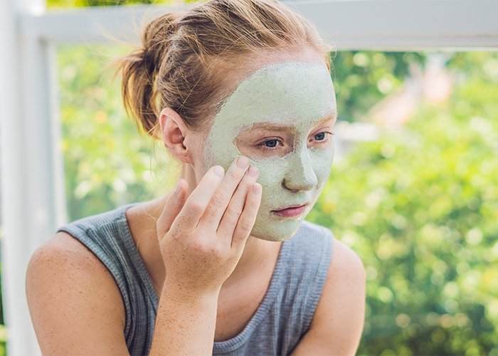Woman applying green homemade face mask for acne