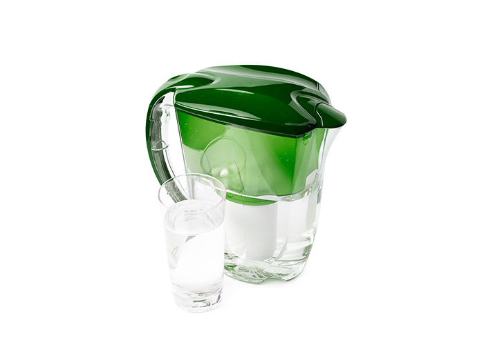green water filtration pitcher next to a glass of water