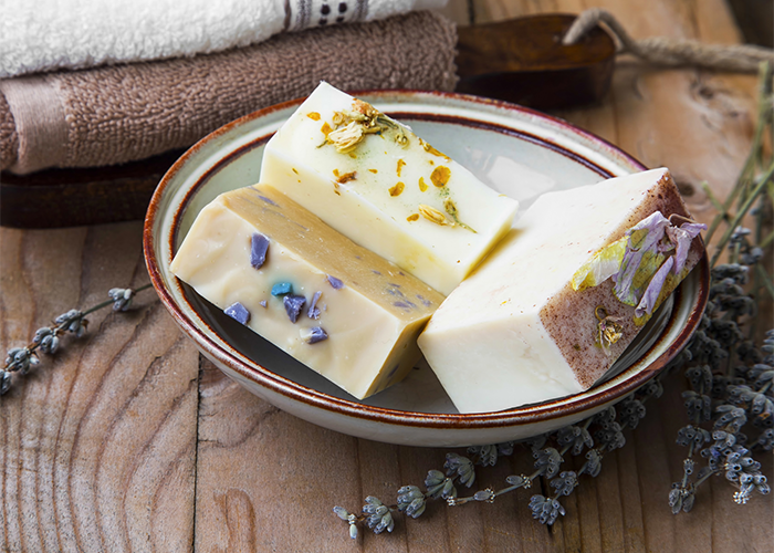 Different goat milk soap bars in a ceramic dish with lavender sprigs around it