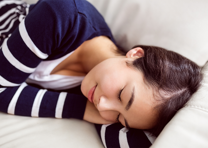 Asian woman smiling with her eyes closed napping on a couch