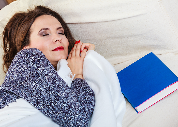 Middle aged woman napping on her couch next to a blue book