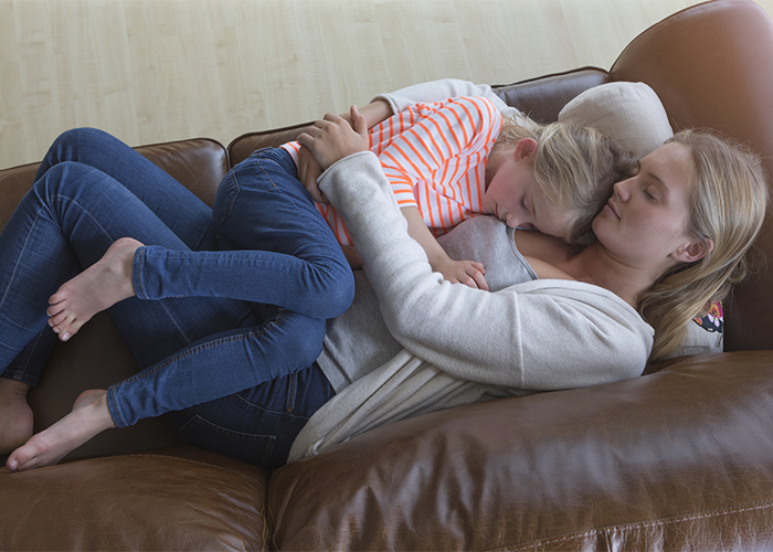 Young mother napping with her daughter in her arms on a brown leather couch