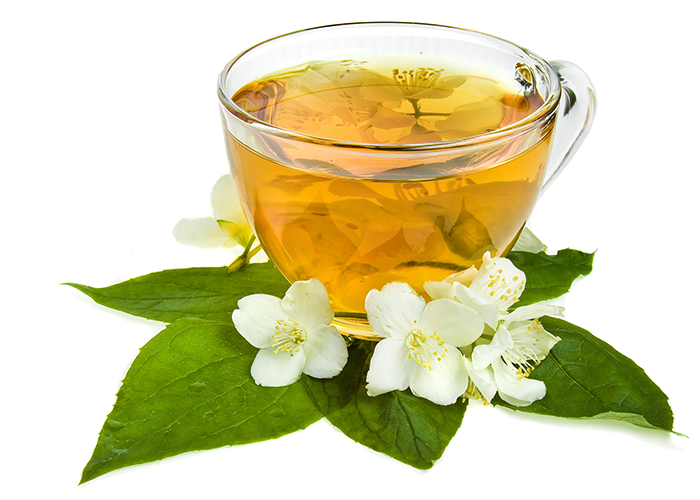 A cup of jasmine tea in a clear teacup laid on green leaves and white jasmine flowers