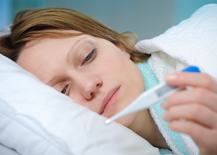 Woman ill in bed with a fever due to lupus holding a thermometer