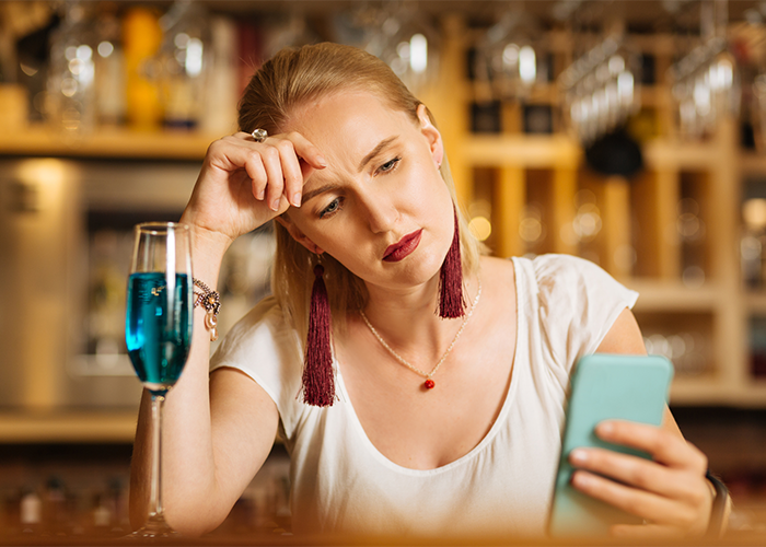 woman in a bar with a drink looking at her phone with a worried look