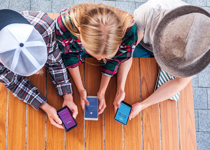 top down view of three friends using social media on their cellphones