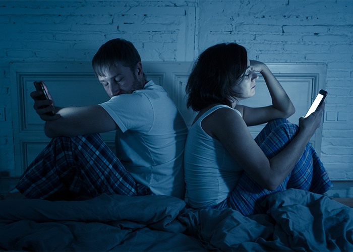 a couple both on their smartphones with their backs to each other in bed