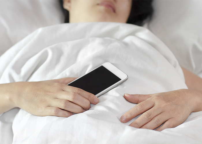 woman asleep in bed holding her smartphone in her hand