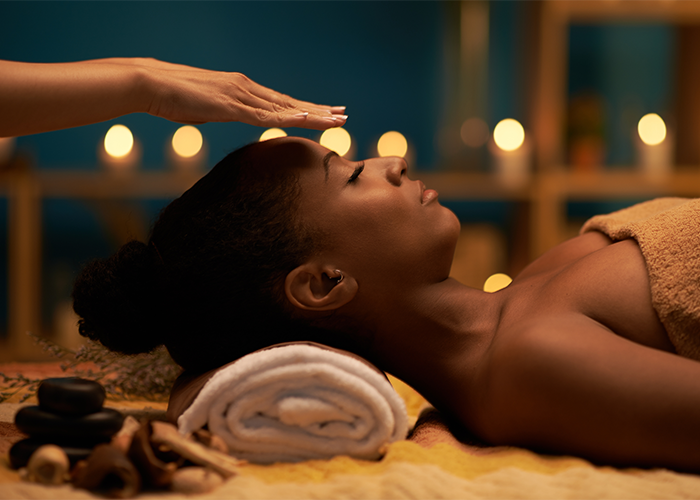 African American woman with eyes closed receiving reiki healing from a practitioner whose hands are floating above her forehead