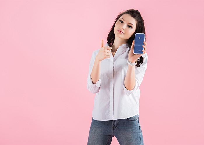 young woman holding a smartphone showing facebook and with her thumbs up