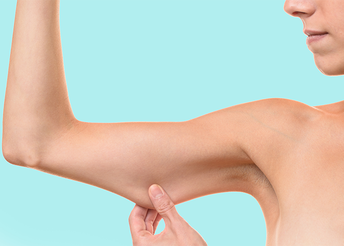 Woman pinching her flabby arm against a pale green background