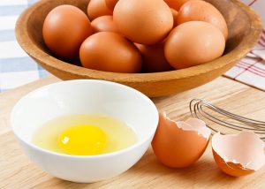 A cracked egg in a bowl next to a bowl of eggs in a bowl