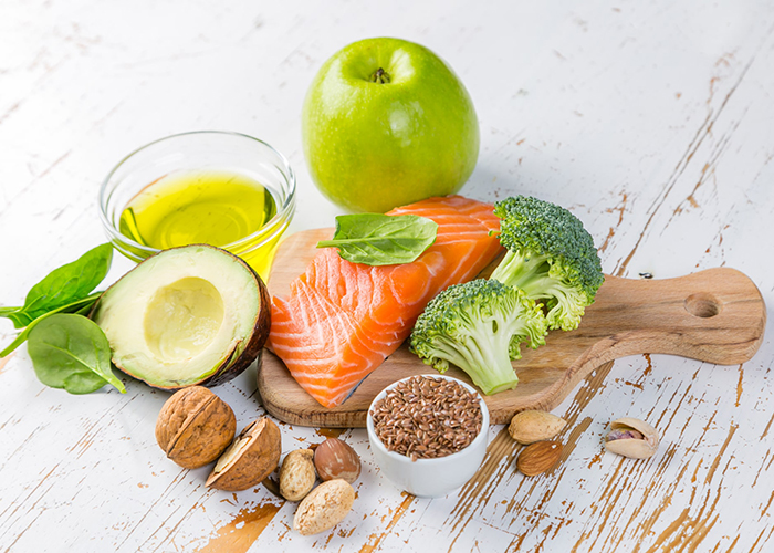 High fat low carb keto diet foods including avocado, salmon, flax seeds, walnuts, an apple, and olive oil