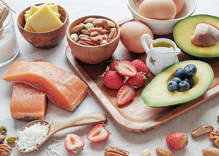 A spread of keto-approved foods that are high in healthy fats and low in carbs such as salmon, cheese, nuts, fruits, eggs, and olive oil