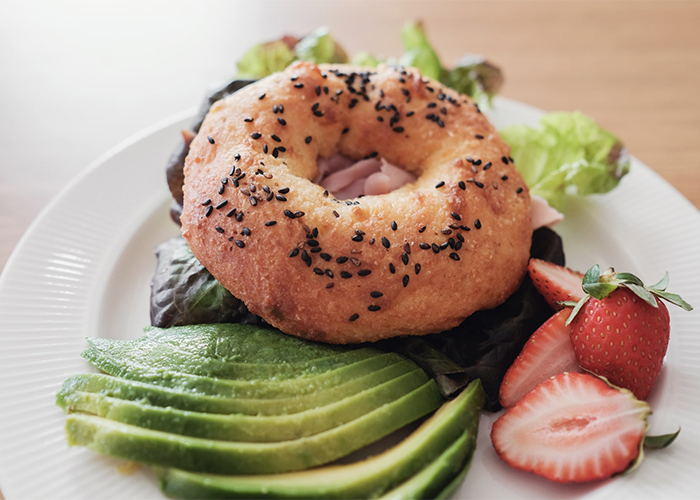 Keto bagel with slices of avocado and ham, with a side serving of strawberries