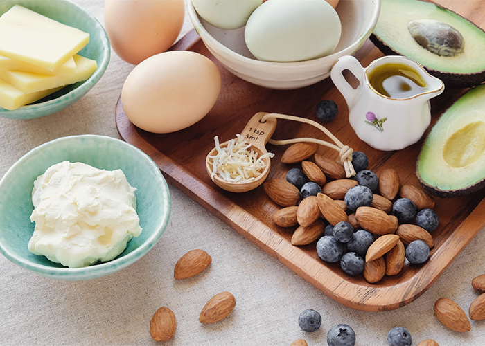 Spread of Ketogenic diet foods including almonds, blueberries, boiled eggs, cream, and avocados