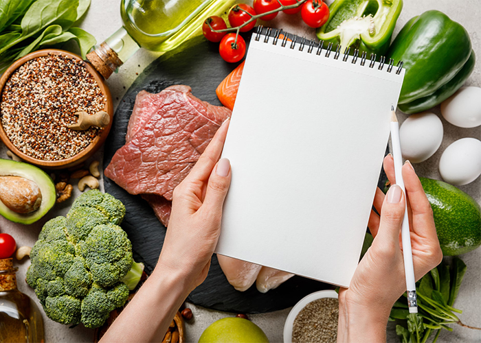 Woman with a blank notepad standing above an assortment of Keto-approved foods about to start ketosis diet meal planning