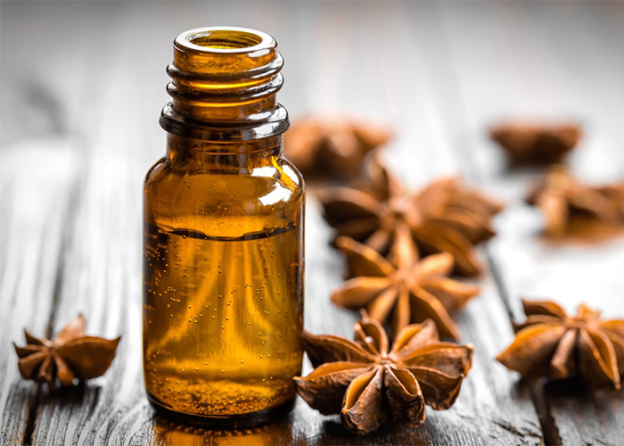 Open bottle of anise essential oil surrounded by dried anise