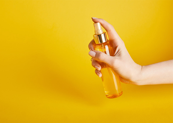 A woman's hand spraying a bottle of orange essential oil mist